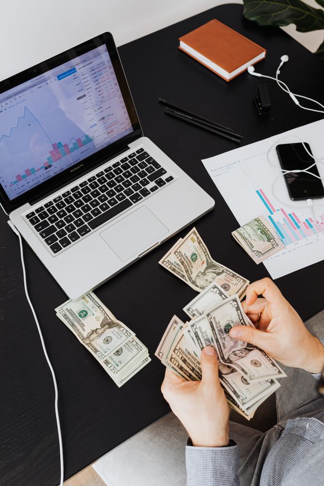 How to Become a Blogger and Earn Money in India: The Short Answer 4 Person counting cash with a laptop analyzing financial trends on a desk.
